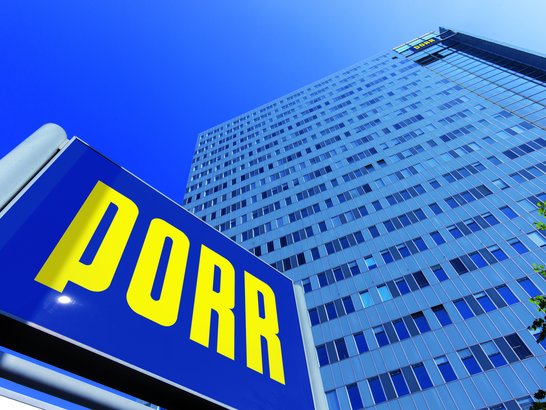 PORR steigt auf Blick von unten auf das Hochhaus der Firma PORR mit PORR Schild davor