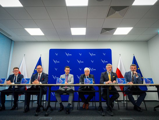 Six men are sitting at a table to sign a contract.
