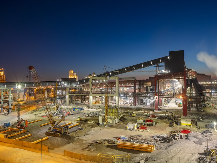 A floodlit building site at night, featuring a crane and steel components