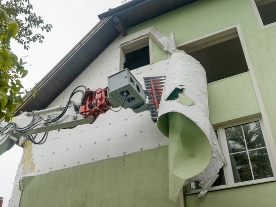 Excavator attachment in action on a house façade