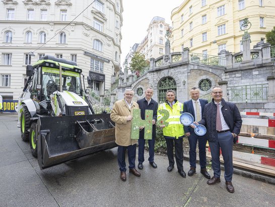 Startschuss fĂŒr das Pilotprojekt CO2-neutraler Bautrupp FĂŒnf Manager vor einem Baggerlader in Wien
